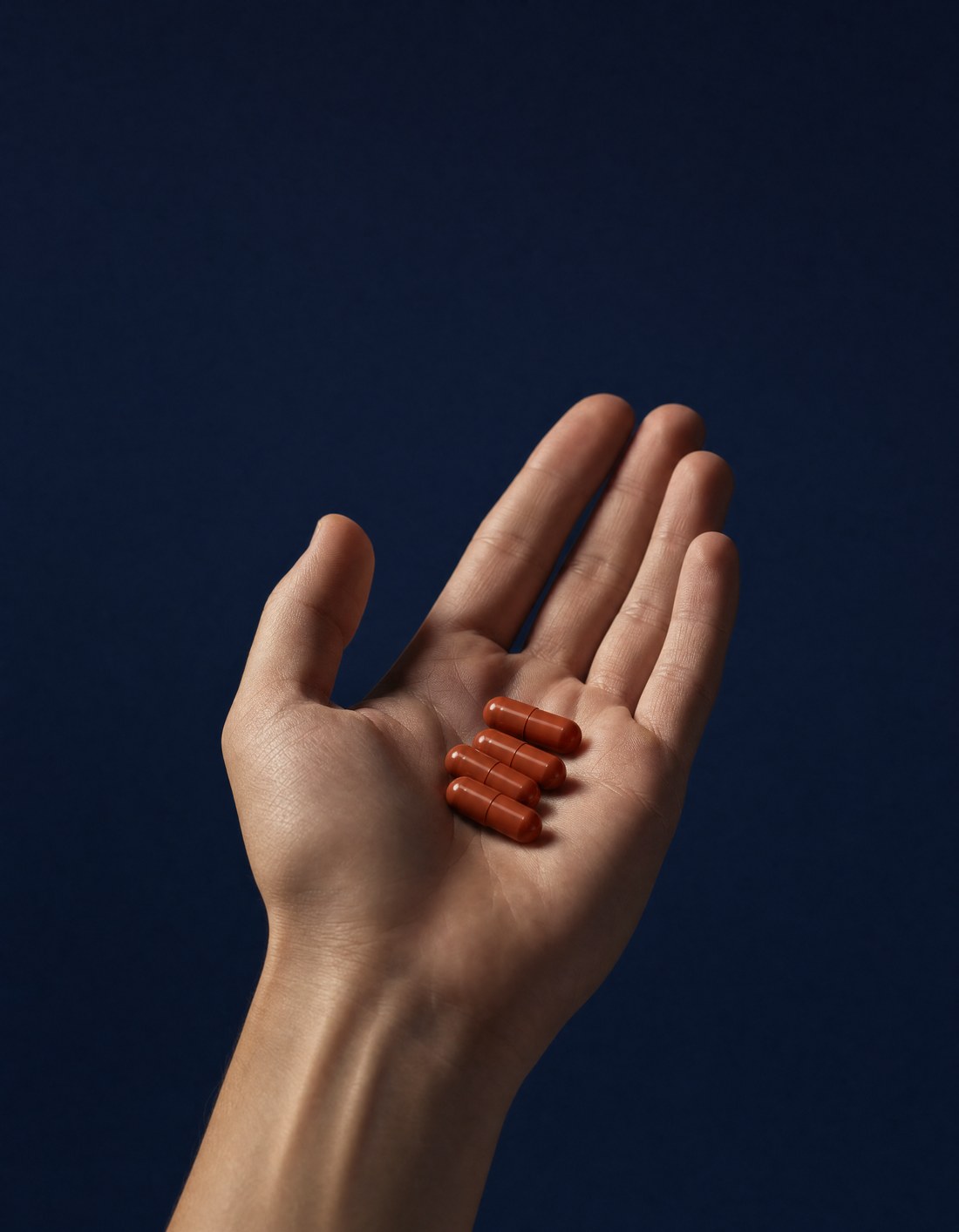 Hand holding four AlphaPeak T1x capsules, the Men's Daily Formula